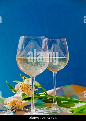Wine glasses with white wine together with flowers and blue background with copy space Stock Photo
