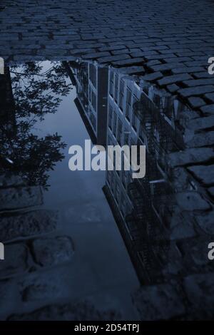 Dark deserted cobblestone backstreet with a puddle reflecting tenement buildings on Crosby Street, SOHO, in New York City. Dark, blue night shadows. Stock Photo