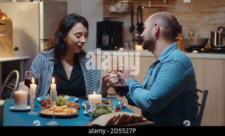 Young cheerful woman being surprised by marriage proposal of her husband. Man making proposal to his girlfriend in the kitchen during romantic dinner. Happy caucasian woman smiling being speechless Stock Photo