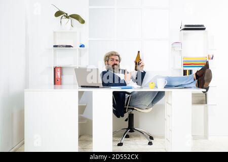 Tired bored businessman yawning at workplace near laptop, boring work, dead end job, overwork extra after hours, drink alcohol. Stock Photo