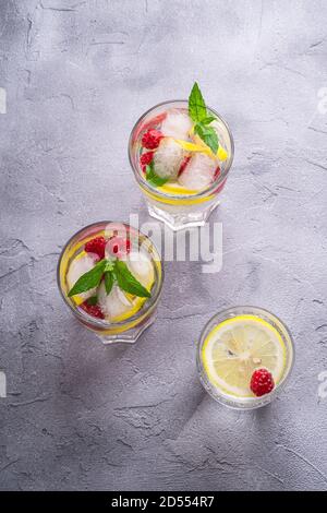 Fresh cold ice water drink with lemon, raspberry fruits and mint leaf in three glass on stone concrete background, summer diet beverage, angle view se Stock Photo