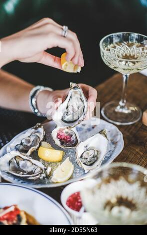 Woman squeezing lemon juice to oysters in plate with ice Stock Photo