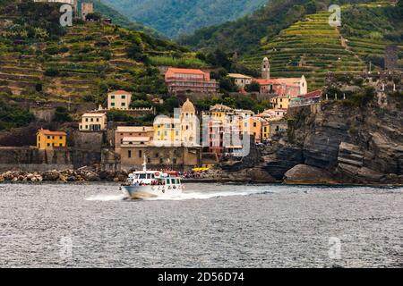 Great close-up view of Vernazza from the sea. A ship with visitors leaves the port. In the background are colourful houses, the Church of Santa... Stock Photo