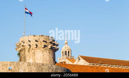 Croatian flag on top of the Large Governors Tower seen in front of the Cathedral of Saint Mark bell tower in Korcula, Croatia in October 2017. Stock Photo