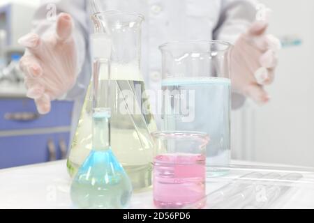 Selective focus of colorful liquid chemicals in glass beaker, flask and tube with scientist hands working. Chemistry Laboratory class experiment background. Stock Photo