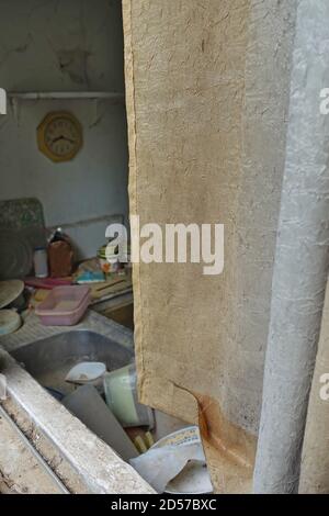 Dirty curtain and kitchen sink with unwashed dishes in abandoned house. Stock Photo