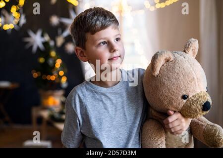 Small boy indoors at home at Christmas, holding teddy bear. Stock Photo