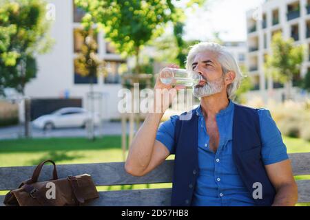Portrait of mature man sitting outdoors in city, drinking water. Stock Photo