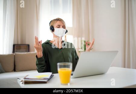 Portrait of business woman indoors in office doing yoga at desk, mental health and coronavirus concept. Stock Photo