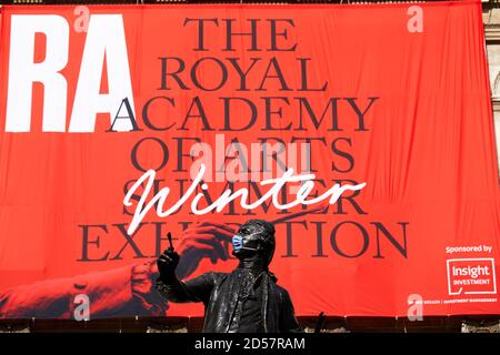 London, UK. - 5 Oct 2020: A masked statue in front of a banner advertising the traditional Royal Academy Summer Exhibition, delayed until October due to the coronavirus pandemic.