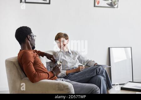 Portrait of young mixed-race couple enjoying champagne while sitting on couch and talking Stock Photo