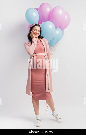 joyful and pregnant woman in dress near balloons on white Stock Photo