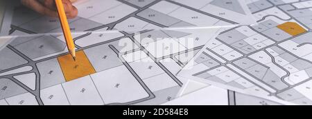 hand with pencil on cadastral map - choose and buy a building plot for house construction. banner copy space Stock Photo