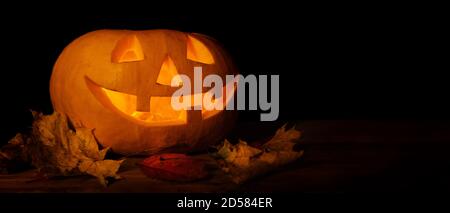 glowing carved halloween pumpkin with autumn leaves on dark background. banner copy space Stock Photo