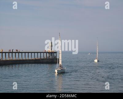 Sail boats arriving at Whitby Harbour in North Yorkshire, England, UK at the end of the day in calm, tranquil conditions. Stock Photo