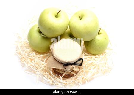 Jar full of cashew and almond nuts near green apples on white background. Farmers summer harvest concept. Nuts and apple pyramid lying on eco straws. Summer time composition. Stock Photo