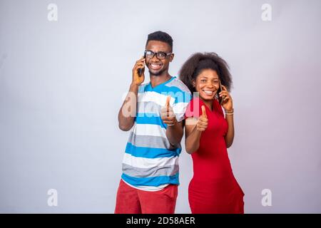 excited young african people making phone calls, standing against a white background, give thumbs up Stock Photo