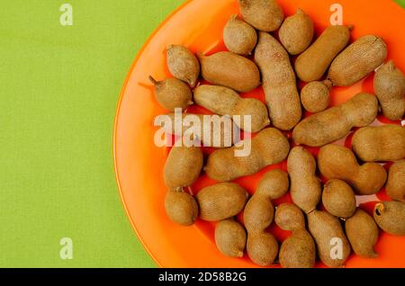 Tamarind, Tamarindus indica pod-like fruit. Contains a sweet, tangy pulp. Placed on a Orange colored plate Stock Photo