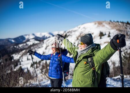 Senior couple hikers with nordic walking poles in snow-covered winter nature, stretching arms. Stock Photo