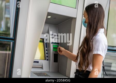 Businesswoman with protective mask is using ATM machine to withdraw cash. Covid-19 virus pandemic concept. Stock Photo