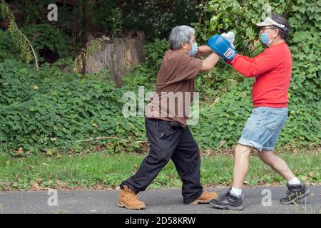 2 middle age men wearing masks  have a boxing workout in a park in Flushing, Queens, New York. Stock Photo