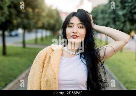 Outdoor close up portrait of young beautiful fashionable Asian brunette lady, wearing stylish accessories and clothes, posing in the city alley with Stock Photo