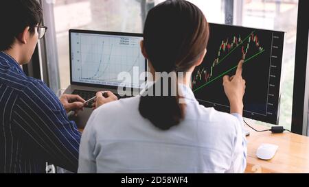 broker showing some ascending to his colleague planning and analyzing graph stock market trading with stock chart data on multiple computer screens Stock Photo