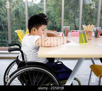 Asian disabled boy on wheelchair drawing picture in art class. Stock Photo