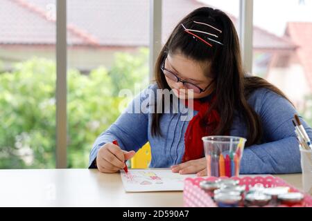 Girl with Down's syndrome drawing picture with crayon in art class. Concept disabled kid learning. Stock Photo