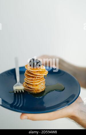 Man's hand holding a plate with a stack of miniature pancakes topped with blackberries and honey Stock Photo