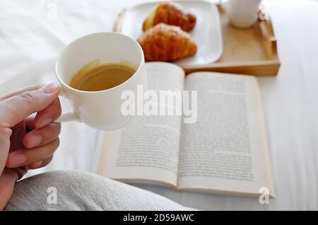 Woman sitting on a bed reading at breakfast Stock Photo