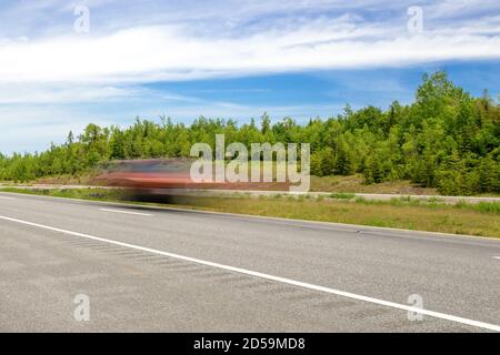 Fast moving red car on a highway. Car is just a blur due to long exposure. Trees in background, partially cloudy sky. Stock Photo