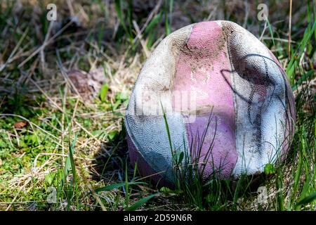 An old, faded, and deflated basketball lying in grass. Part shade and part sunlight on the ball. The ball is also dirty. Stock Photo