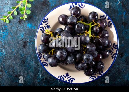 Fresh black grapes and leaves in dish on dark background. Stock Photo