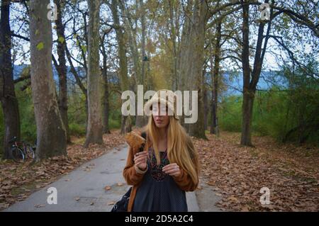 Portrait of a girl looking thoughtfully at a leaf, surrounded by trees and leaves, autumn, walk in the linden alley. Stock Photo