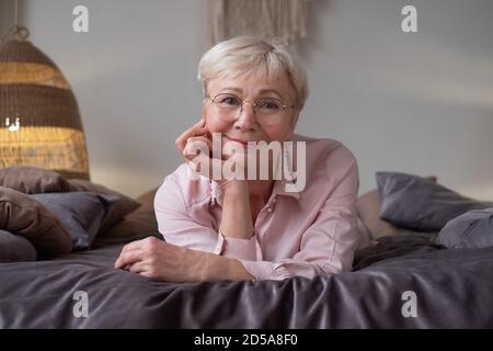 Senior caucasian woman relaxing on bed smiling at camera Stock Photo