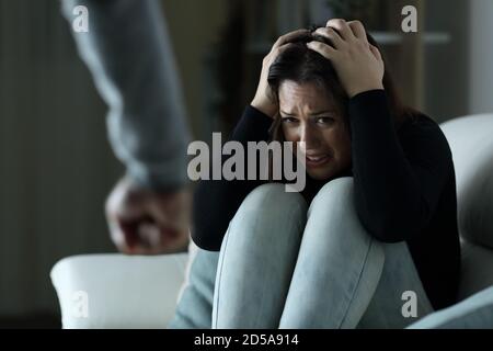 Scared woman victim of gender violence sitting on a couch in the night at home Stock Photo
