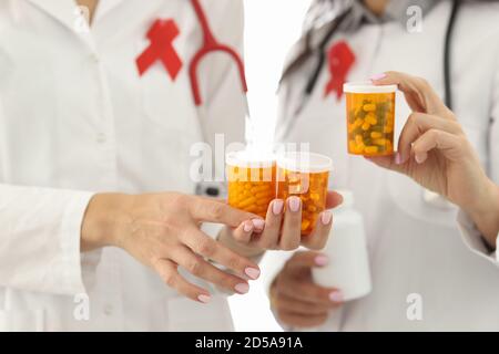 Doctors with red ribbon on uniforms are holding jars of medicines closeup Stock Photo