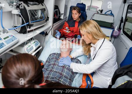 Selective focus of doctor in latex gloves doing cardiopulmonary resuscitation to patient near paramedics in ambulance car Stock Photo
