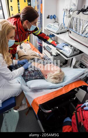 Selective focus of paramedic and doctor in medical masks examining patient with stethoscope in ambulance car Stock Photo