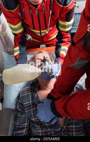 Top view of paramedics in latex gloves doing cardiopulmonary resuscitation to senior man in ambulance auto Stock Photo