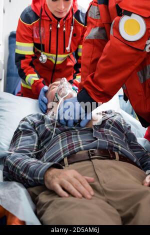 Selective focus of paramedics in latex gloves doing cardiopulmonary resuscitation to patient in oxygen mask Stock Photo