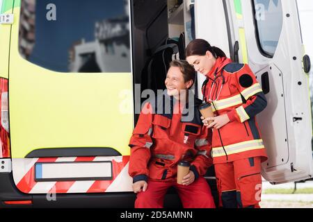 Paramedics in uniform holding coffee to go near ambulance car Stock Photo