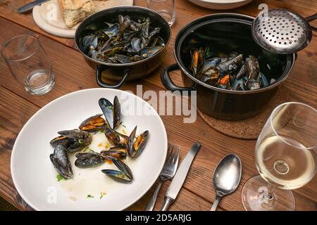 Blue mussels in the traditional French pot, plates, glasses and cutlery on a rustic wooden table while having an informal meal with family or friends, Stock Photo