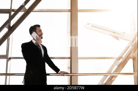 Cheerful businessman standing in airport, talking on phone Stock Photo