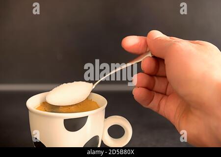 Hand holding a spoon, adding sugar to coffee. Stock Photo