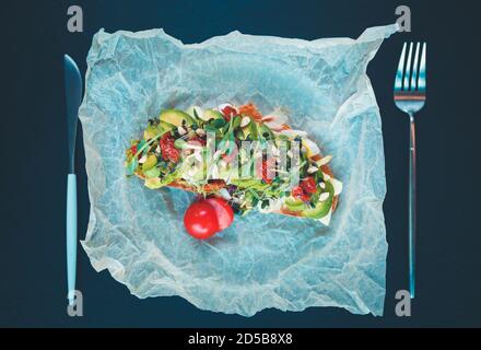 Avocado toast served for lunch on crafted parchment paper in vegetarian restaurant with fork and knife,shot directly from above on table.Delicious veg Stock Photo