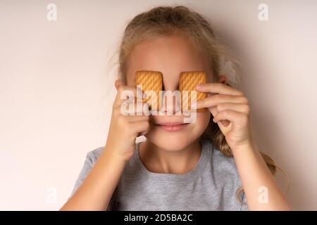 Full of sweet taste. Cute little girl having fun with cookies. The beautiful girl covered her eyes with cookies. Bakery-style cookie recipe. Stock Photo