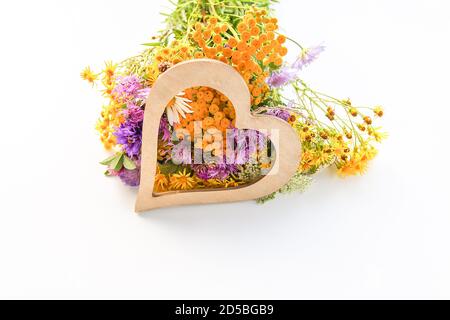 Bouquet of tansy, white daisy and thorny burdock wild summer flowers with wooden decorative heart Stock Photo
