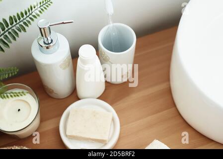 White toothbrush, liquid soap in the dispensary, natural soap, aroma candle over white wall near sink. Stock Photo